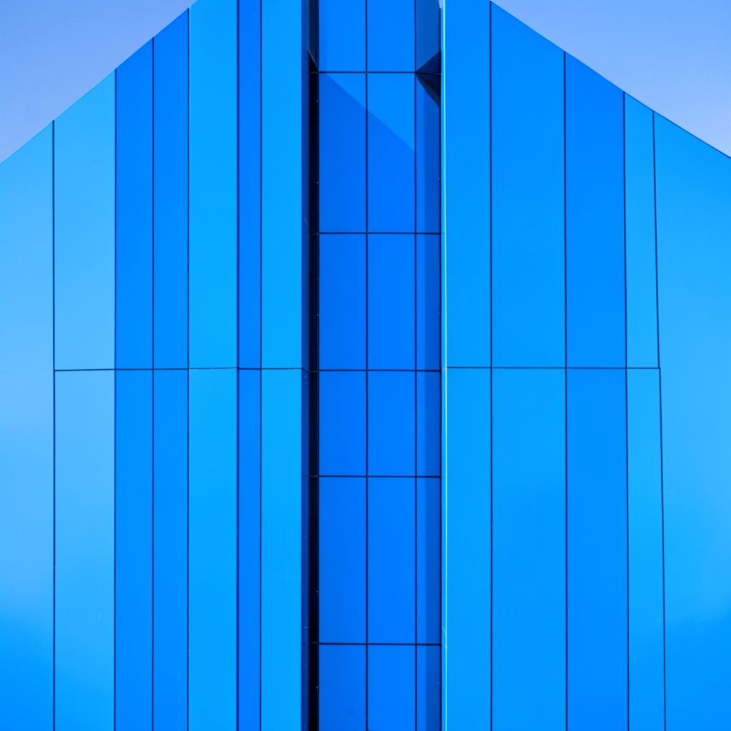 Fachada del espacio cultural Las Naves en Valencia, edificio de líneas modernas con grandes ventanales y una plaza abierta al frente, bajo un cielo azul despejado.