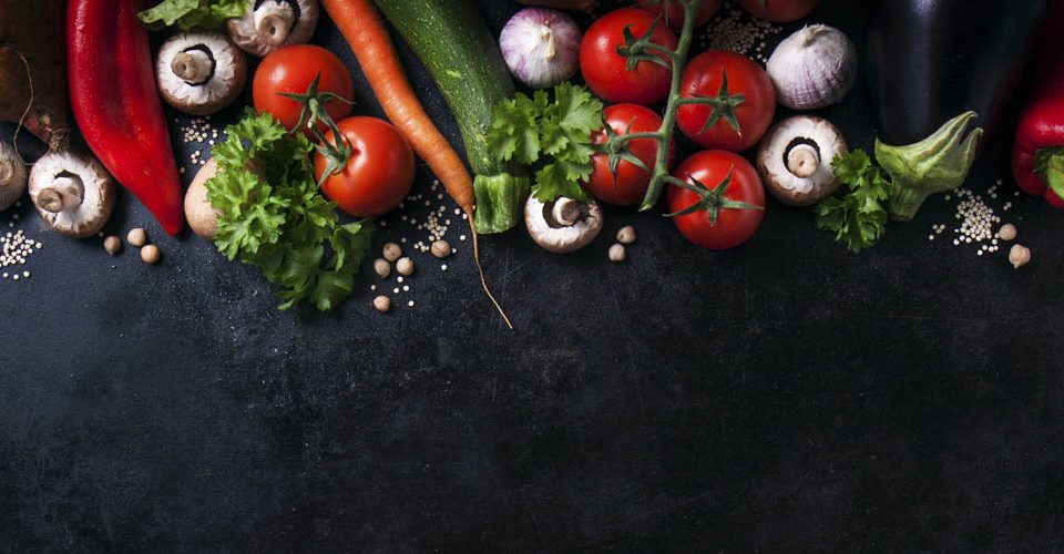 Composición cenital de verduras frescas como tomates, champiñones, zanahoria, calabacín, ajo y pimientos sobre una superficie oscura
